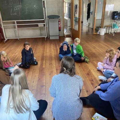 Kinder im Sitzkreis hören einer Studentin zu