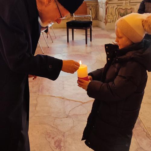 Herr Abt German zündet eine Kerze an, die ein Mädchen hält